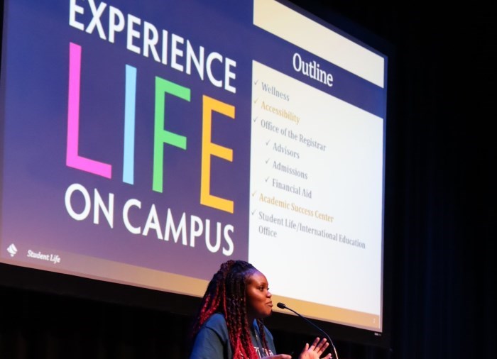 Photo of Student Life representative on stage with "experience life on campus" on the screen behind her.