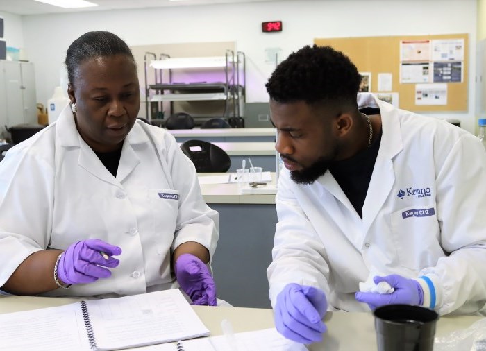 an older woman and young man in a lab wearing labcoats and latex gloves working on a science experiment